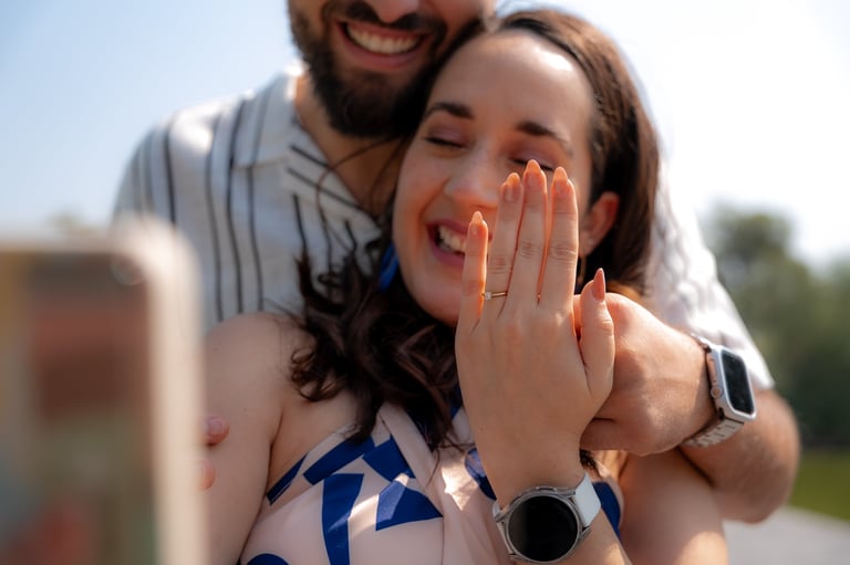 Pareja posando al aire libre con la mujer mostrando el anillo de compromiso en su mano izquierda