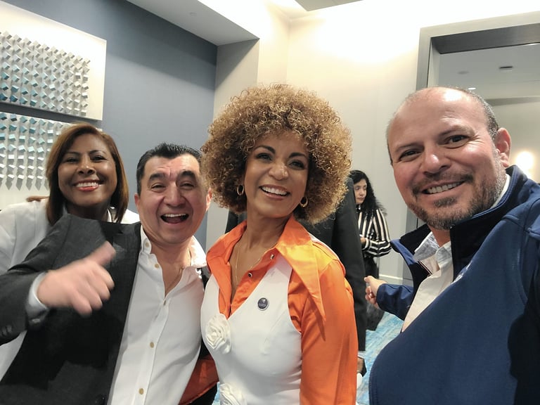 Four people smiling at the camera in an indoor venue, with one woman in an orange and white jacket in the center