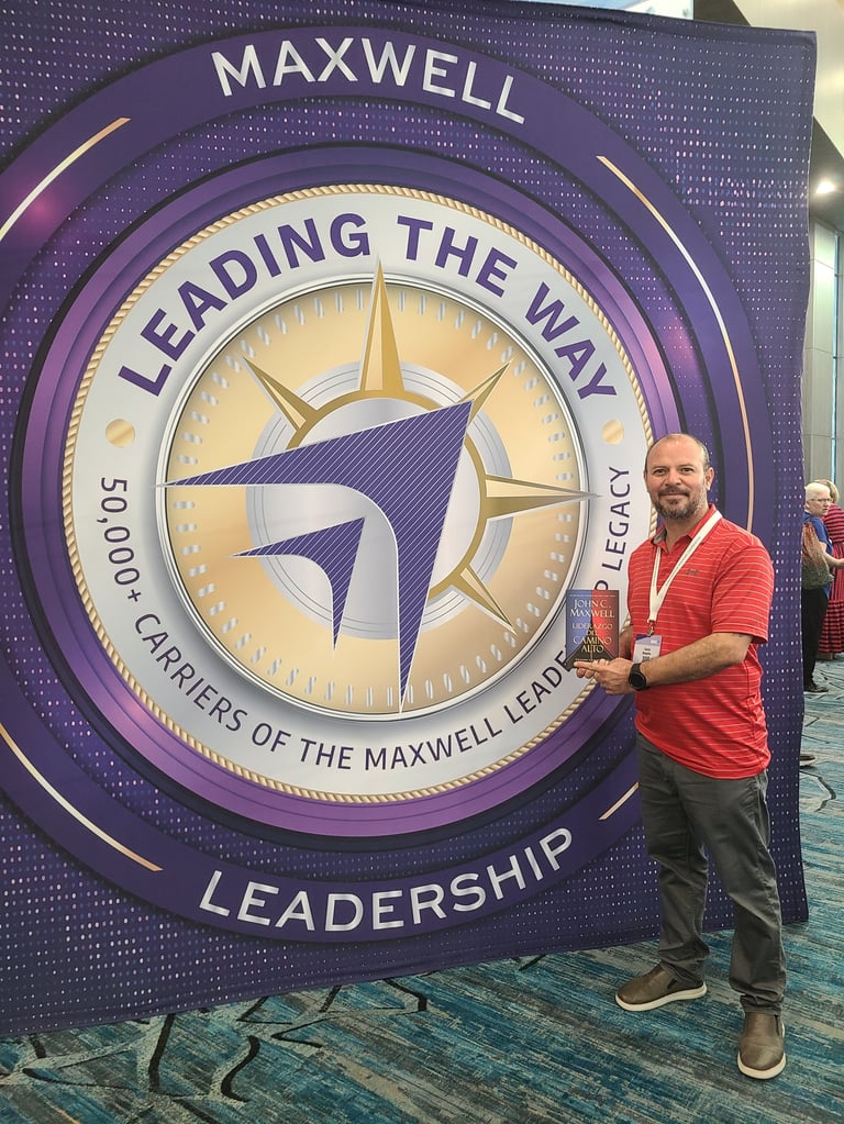 Man in red shirt standing next to large purple Maxwell Leadership banner with compass logo and Leading the Way text