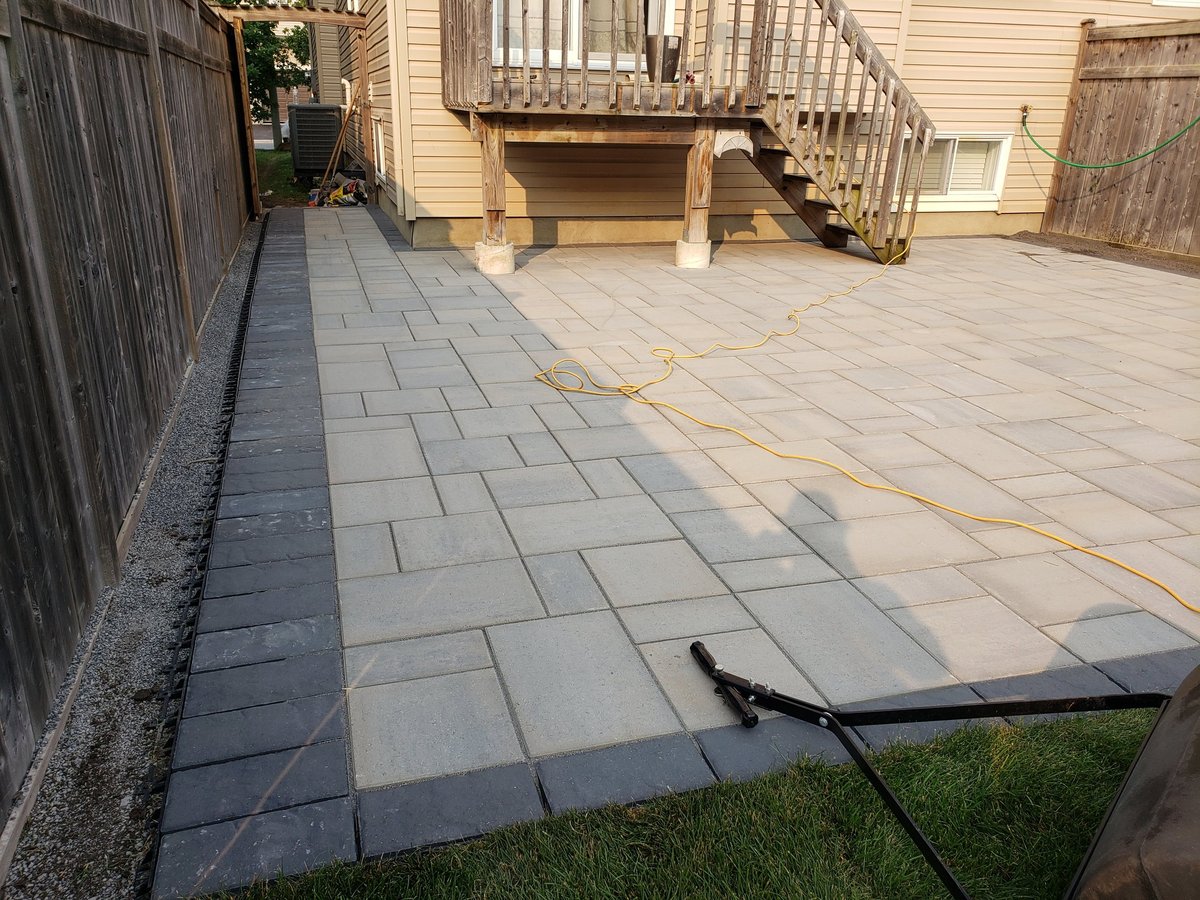 Newly installed gray paver patio with wooden deck and stairs in a residential backyard