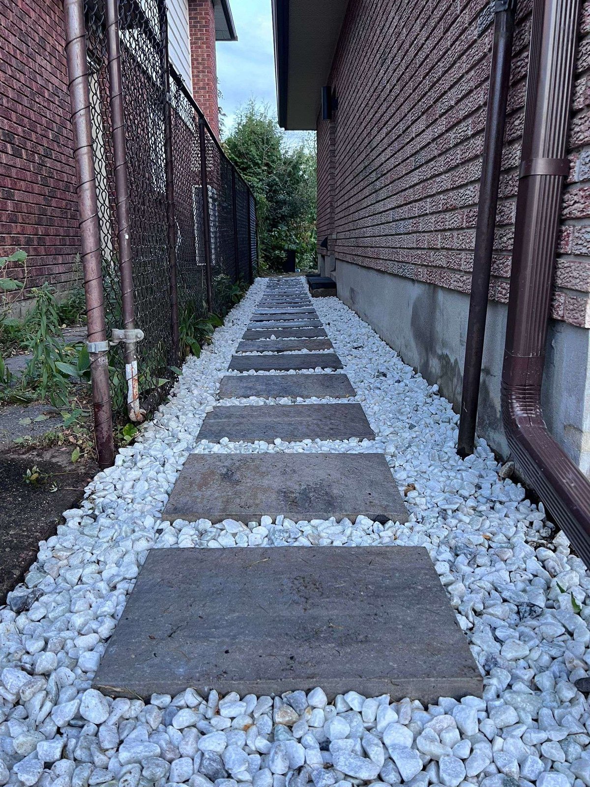 Narrow alley with dark stepping stones embedded in white gravel between brick buildings