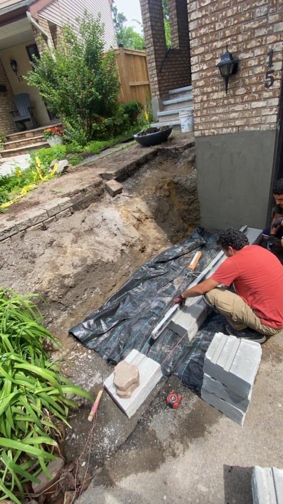 Worker in red shirt laying landscape fabric for yard construction project near brick house