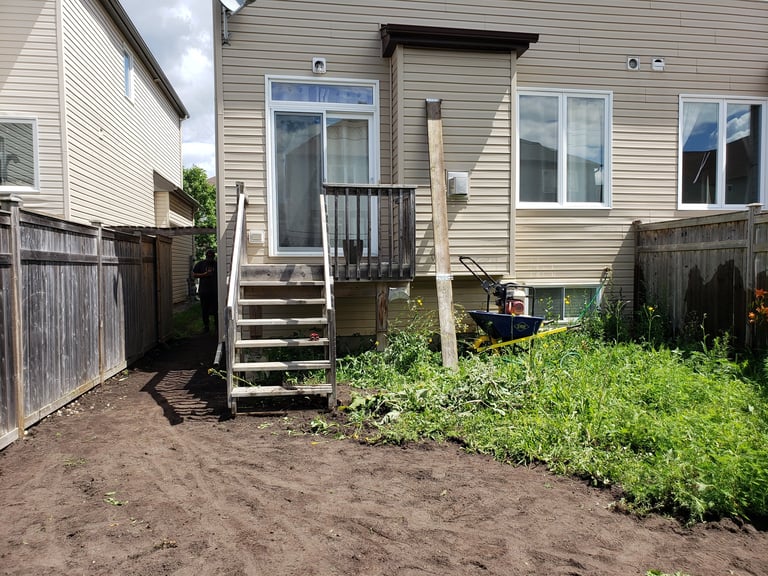 Beige residential house with deck and wooden fence surrounding overgrown backyard with dirt ground