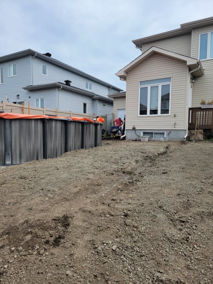 Two suburban homes on gravel lot with metal storage shed and construction materials during landscaping project