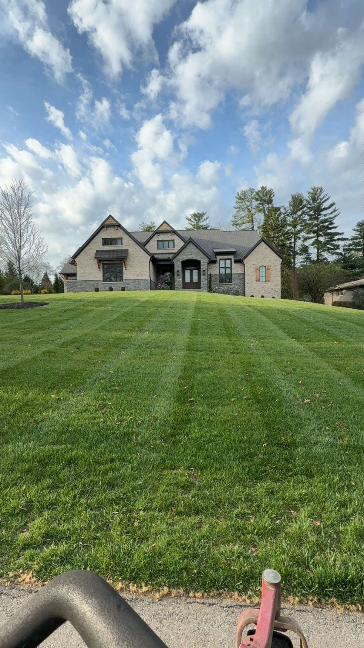 Modern two-story residential home with stone and brick facade on manicured green lawn under blue sky with white clouds
