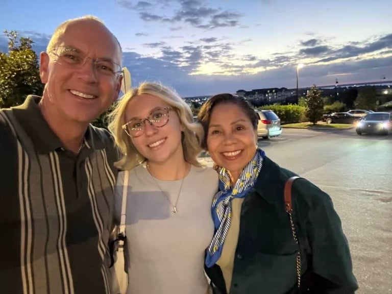 Three people smiling at sunset by a river with a city skyline in the background