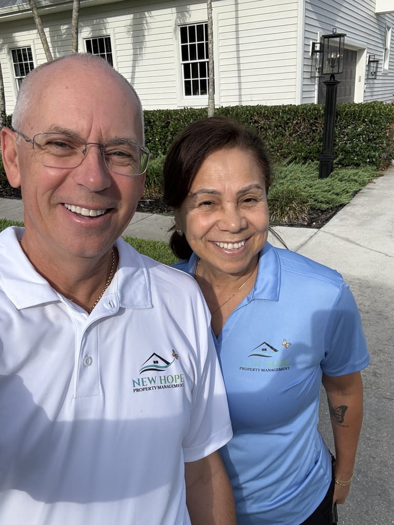Two people smiling at camera wearing polo shirts with company logos in front of a white house and driveway