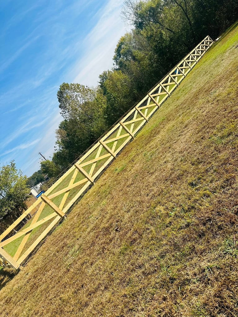 Yellow farm equipment tractor boom extends across grassy field with trees under blue sky