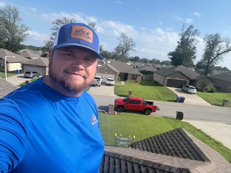 Zackary, Co-Founder of North Slope Exteriors, on a residential roof in his NSE cap and shirt with the company red truck below