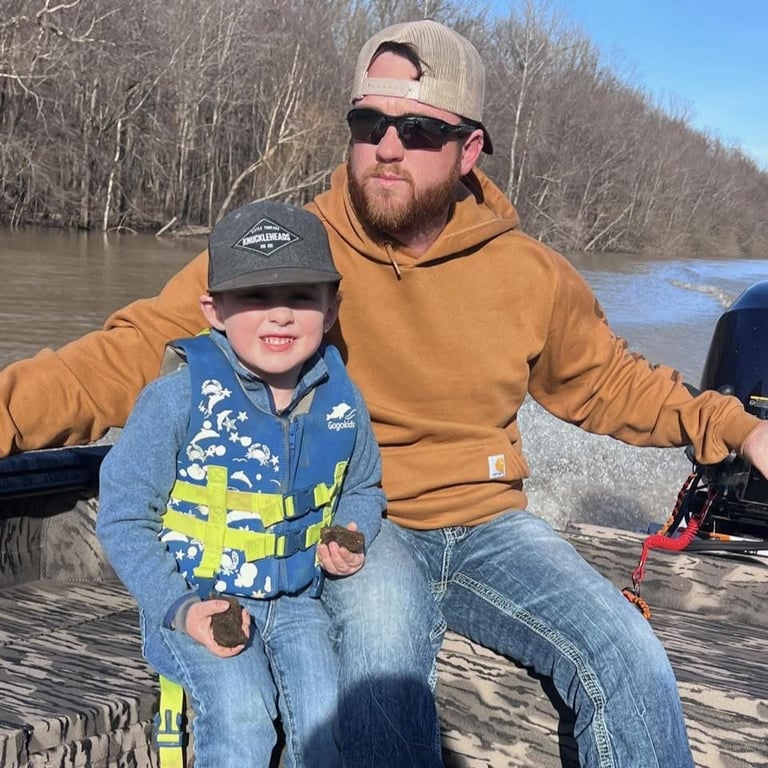 Spencer, Roof Inspector at North Slope Exteriors, on a boat with a child against a river backdrop