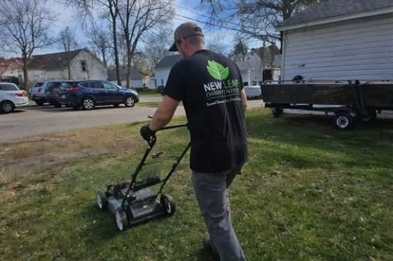 Man in black shirt using a ground penetrating radar device on a residential lawn with parked cars and a trailer in the background