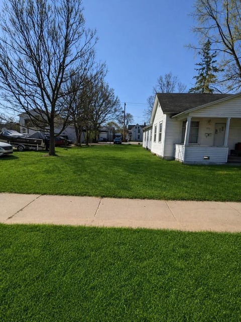White residential house with front porch on a quiet tree-lined suburban street with green lawn and sidewalk