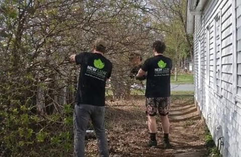 Two people wearing black shirts with green logos jogging on a dirt path between bare trees and a white building