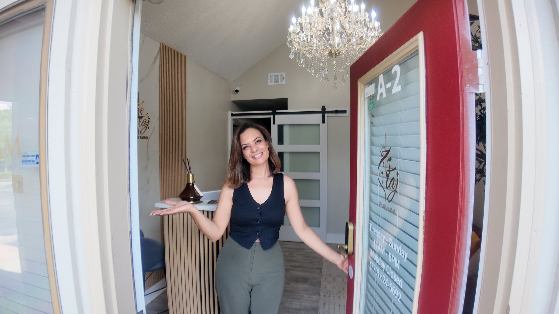 Woman in black vest posing in elegant foyer with chandelier and red-framed doorway