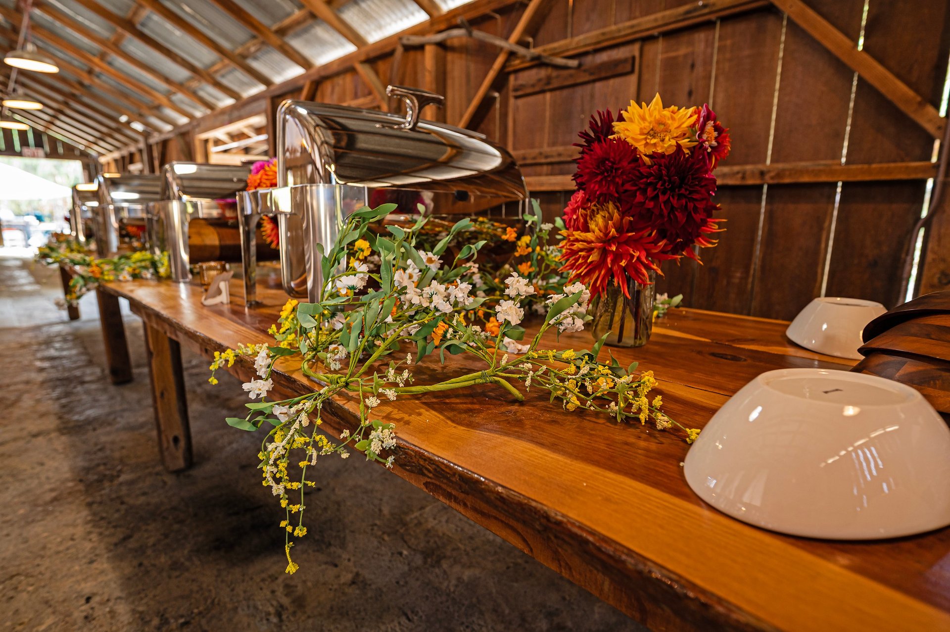 Wooden table with red and yellow dahlia flower arrangement and white bowls in a rustic barn setting