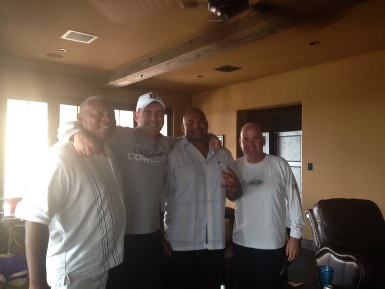 Four men standing together indoors in a casual group pose
