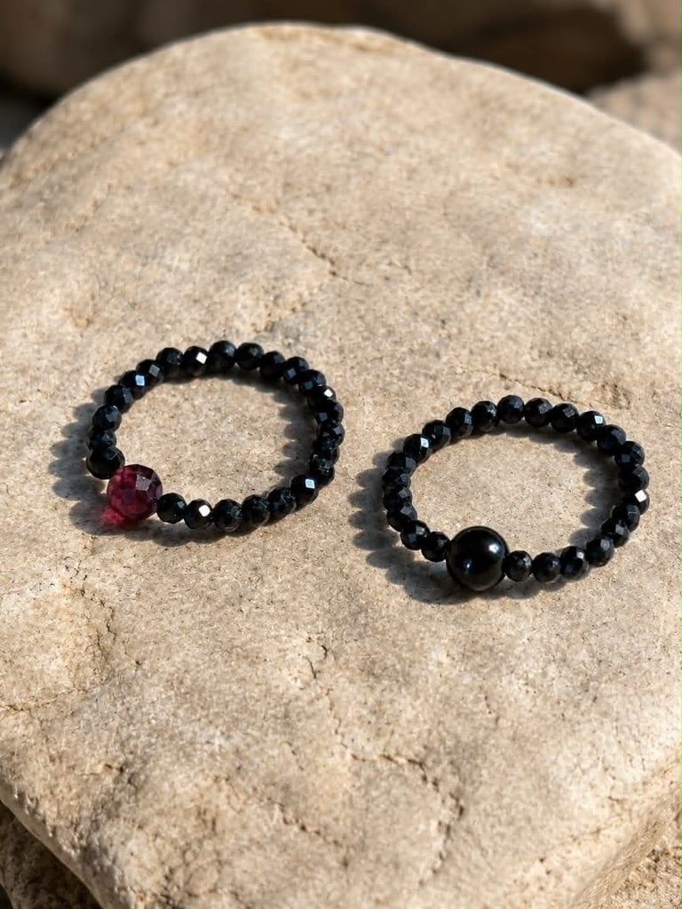 Two black beaded bracelets on a beige stone, one with a red garnet centerpiece and one with a black onyx stone