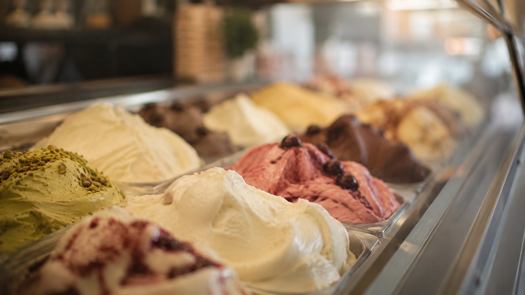 Display case of colorful gelato flavors including pistachio, vanilla, and strawberry in metal containers