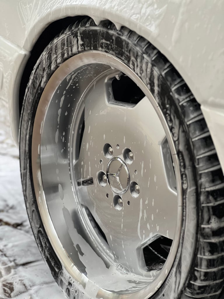 Close-up of a car wheel and tire with white plastic protective covering, showing a silver multi-spoke alloy rim covered in dust and debris