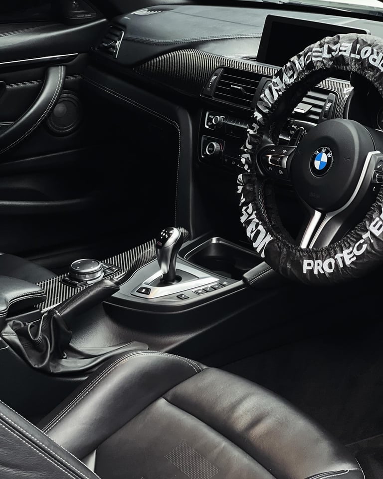 BMW car interior with steering wheel covered in white protective bag, black leather seats, and dashboard controls