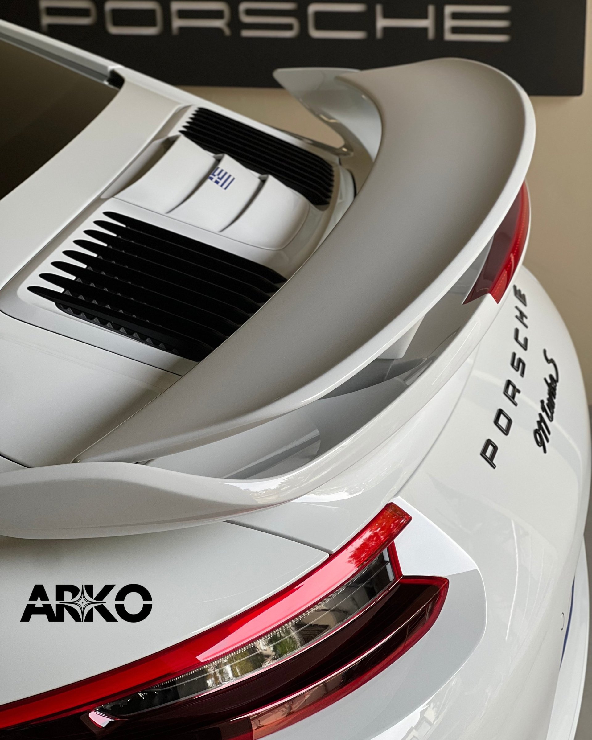 Close-up of white Porsche 911 model car showing rear spoiler, red taillights, and ARKO detail on side