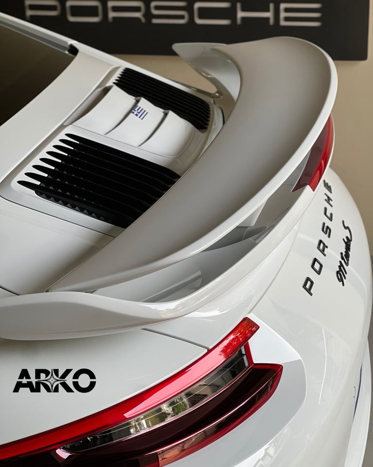 Close-up of white Porsche 911 model car showing rear spoiler, red taillights, and ARKO detail on side