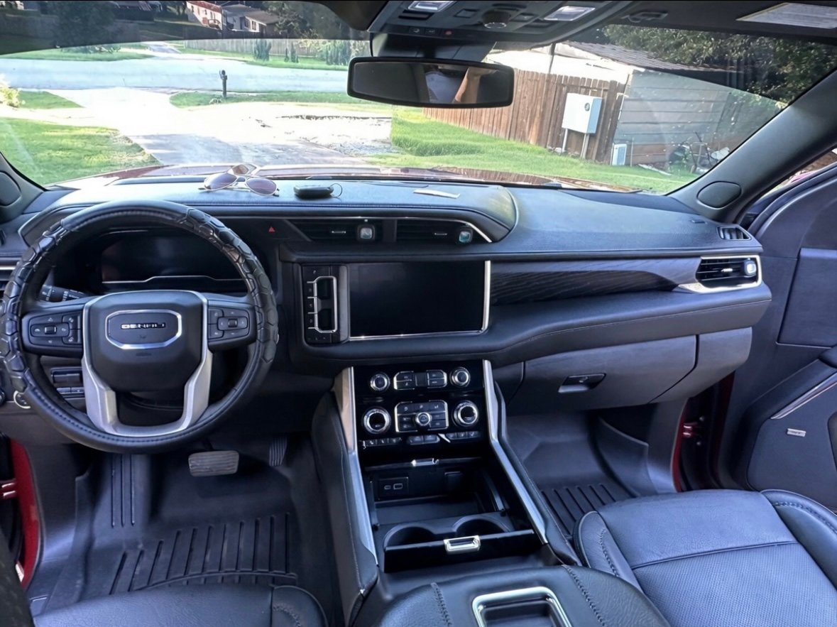 Interior view of a modern SUV showing steering wheel, touchscreen display, dashboard controls, and gray leather seats with outdoor scenery visible through windshield