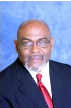 Professional headshot of Berdell Lindsey wearing a dark suit and red tie against a blue background