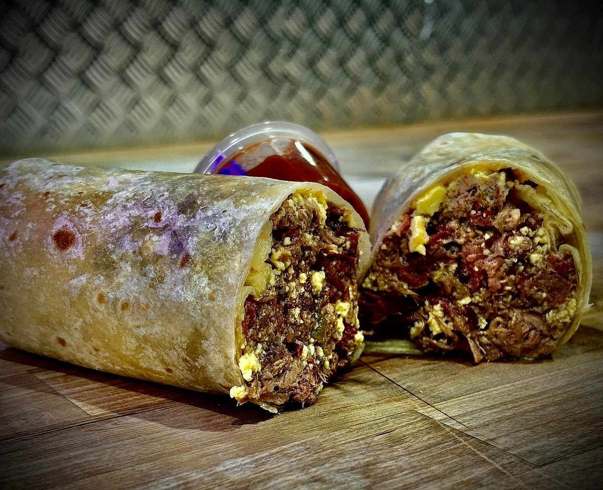 Two burrito wraps cut in half showing meat and vegetable filling inside, placed on wooden surface
