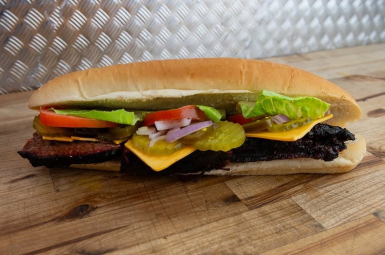 Brisket sub on a hoagie roll loaded with sliced brisket, cheese, lettuce, tomato, pickles, onion and jalapeños on a wooden surface