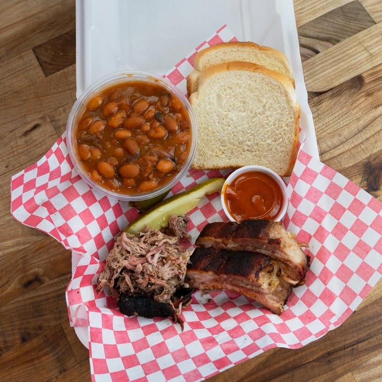 2 Meats Box with pulled pork, fries, coleslaw, white bread, and barbecue sauce on red-checkered paper