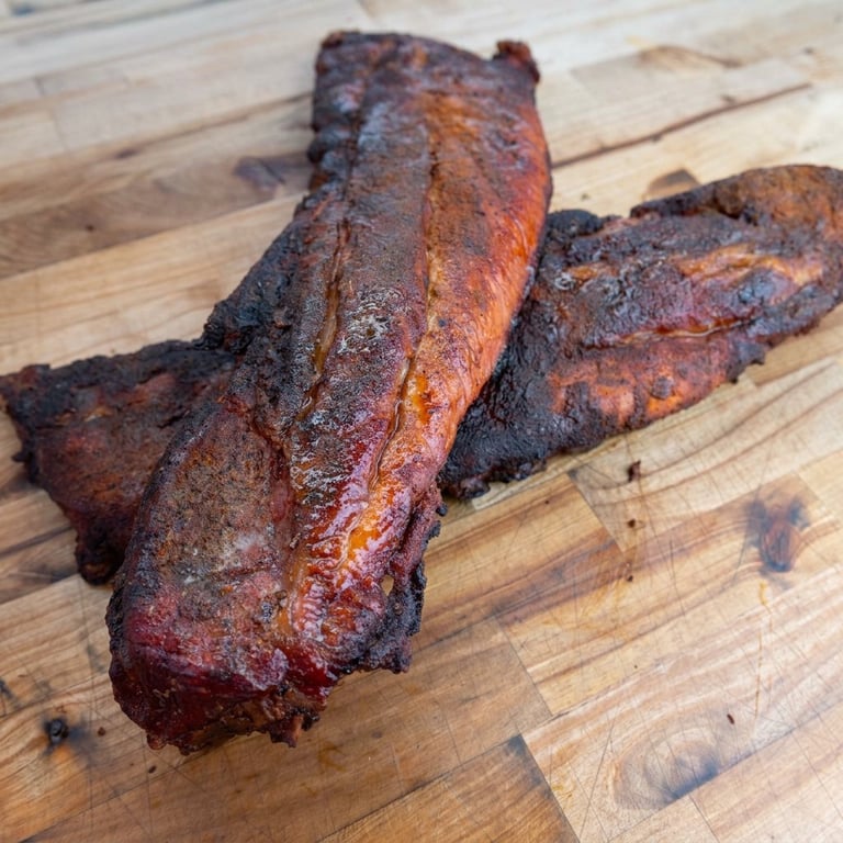 Two smoked beef brisket ribs with dark bark crust on a wooden cutting board