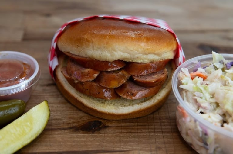 Bacon sandwich with crispy strips on a toasted bun, served with coleslaw, pickle, and sauce on a wooden surface