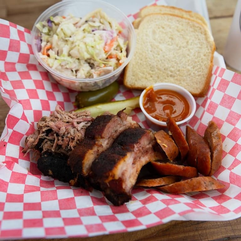 3 Meats Box with pulled pork, fries, coleslaw, white bread, and barbecue sauce on red-checkered paper
