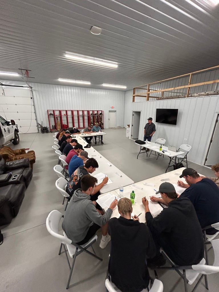 Group of people seated around a long table in a warehouse-style room, appearing to participate in a community meeting or event.