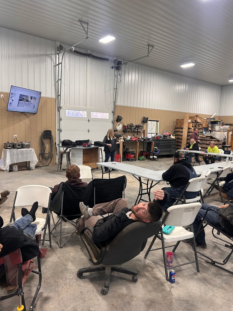 People sitting in chairs in an industrial warehouse workshop space with equipment and work tables visible