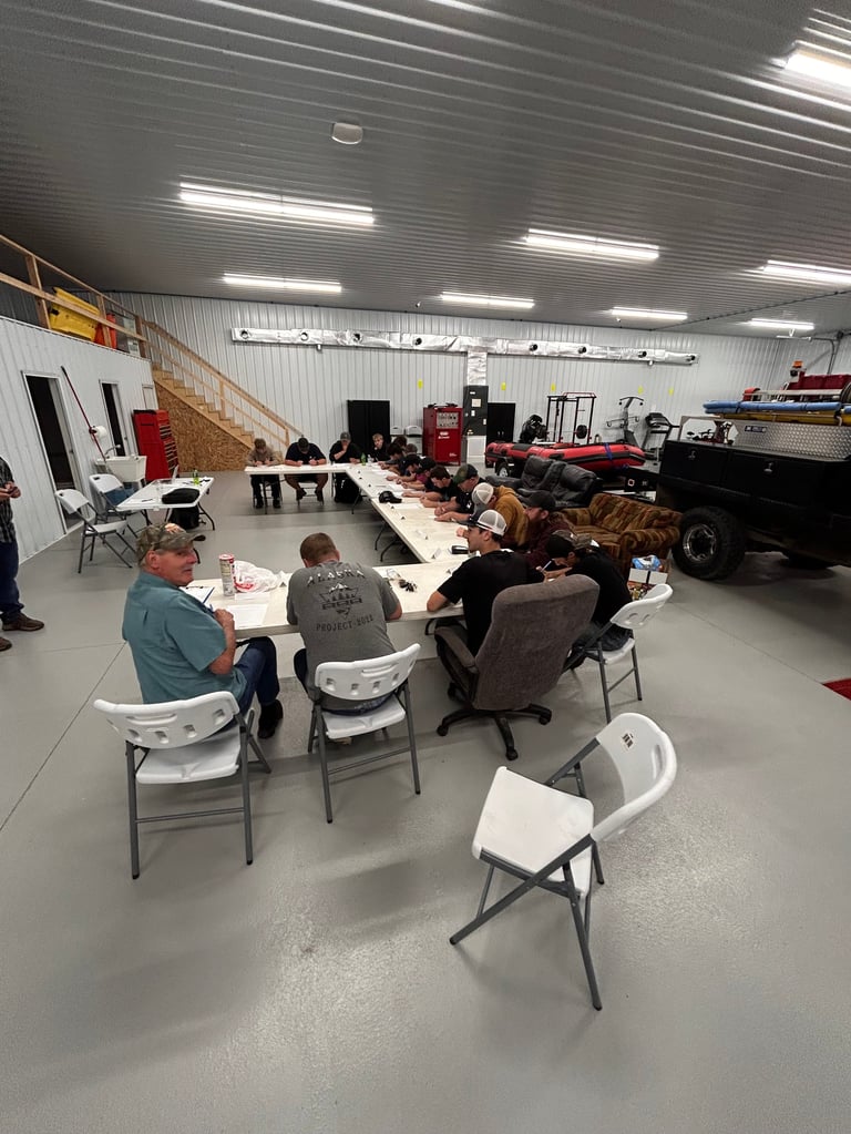 Group of people seated around tables in an industrial warehouse space with concrete floor and metal ceiling fixtures.