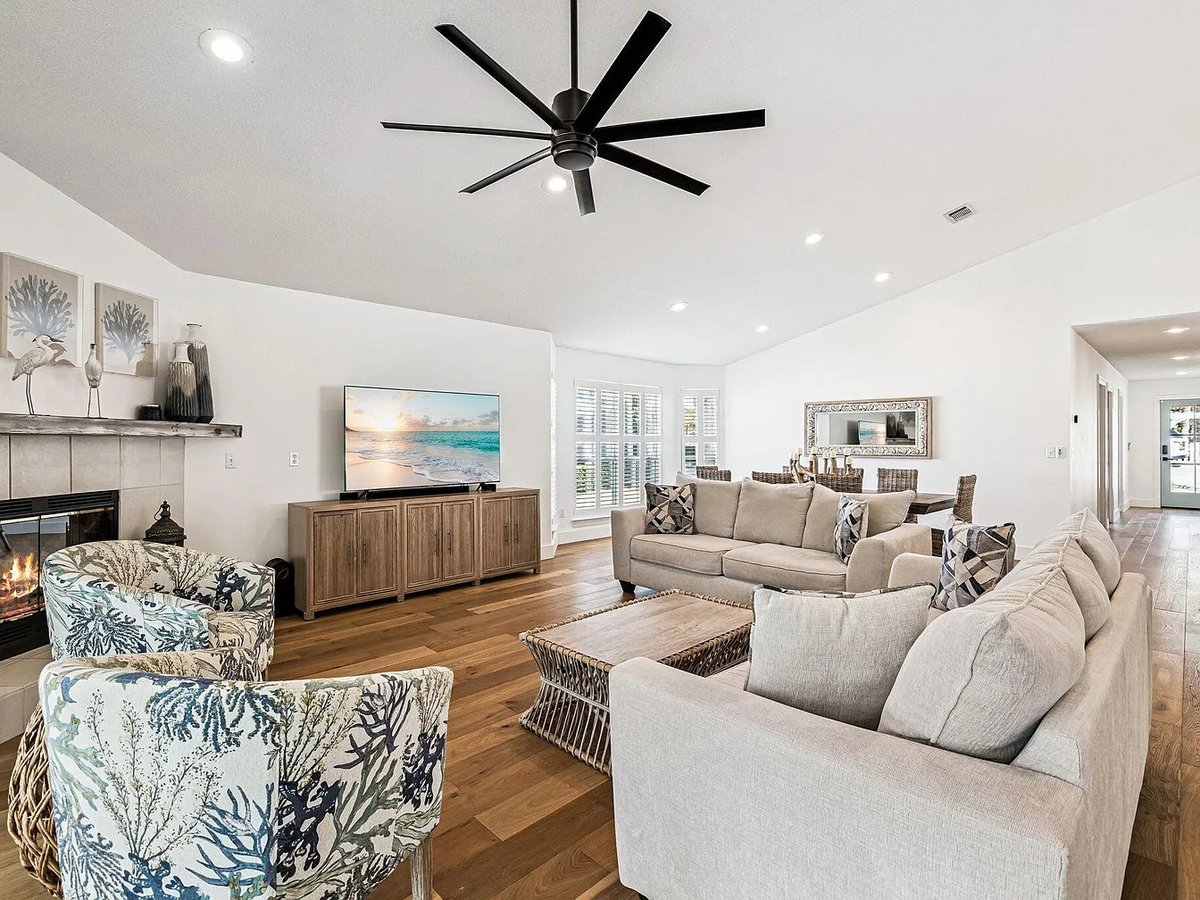 Modern living room with neutral furniture, wood media console, black ceiling fan, fireplace, and hardwood floors