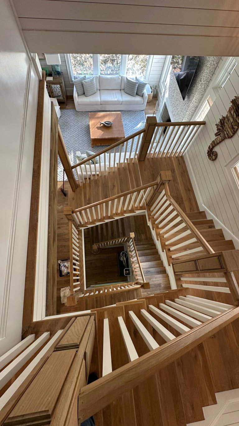 Overhead view of a wooden staircase descending through multiple levels of a modern home with a cream-colored sofa and large windows visible above