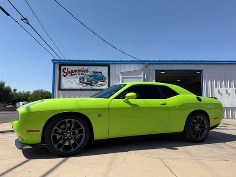 Bright lime green Dodge Challenger parked outside a auto shop with clear sky and power lines