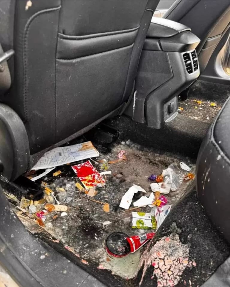 Dirty car floor with accumulated trash, crumbs, and scattered debris between front and back seats