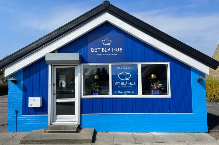 Bright blue small building with white trim, featuring a central door and windows, with Det Blå Hus signage visible