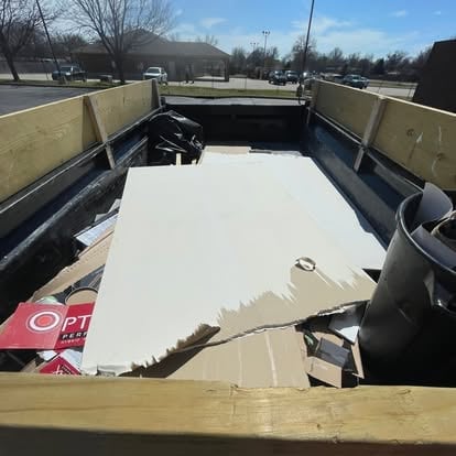 Empty utility trailer bed with white tarp covering items, parked in an outdoor lot on a clear day