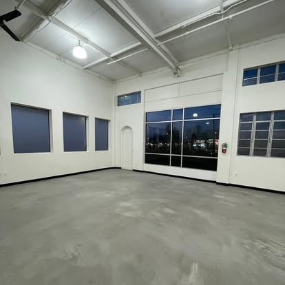 Empty modern warehouse or commercial space with polished concrete floor, white walls, and large windows with dark frames