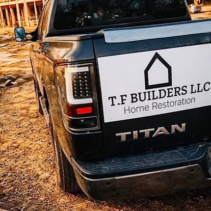 Nissan Titan truck with T.F Builders LLC Home Restoration logo on the tailgate, parked at a construction site