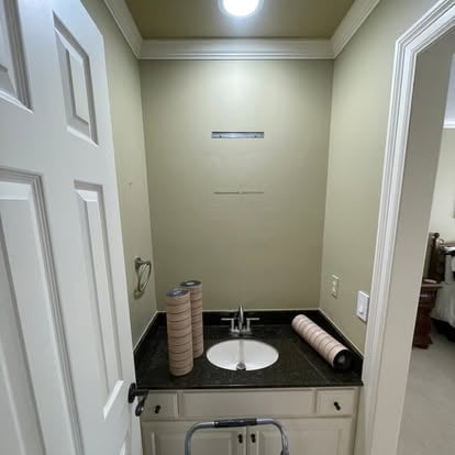 Small bathroom with beige walls, white cabinets, black countertop, round sink, and paper towel dispenser