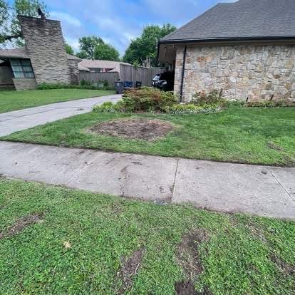 Residential front yard with concrete driveway, green grass, landscaping beds, and stone house with chimney