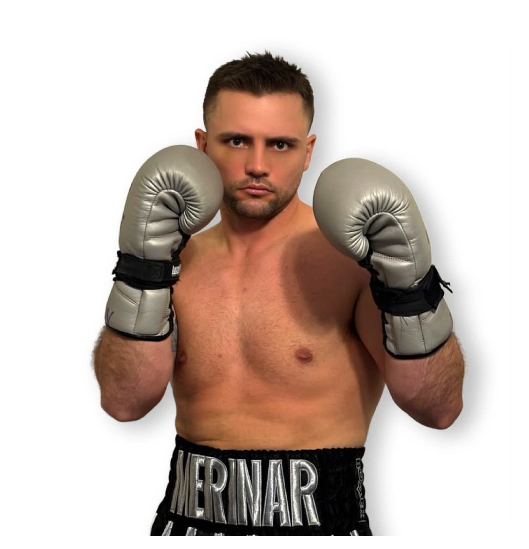 Jon Merinar in gray and black boxing gloves in ready stance, wearing black shorts with his name on the waistband