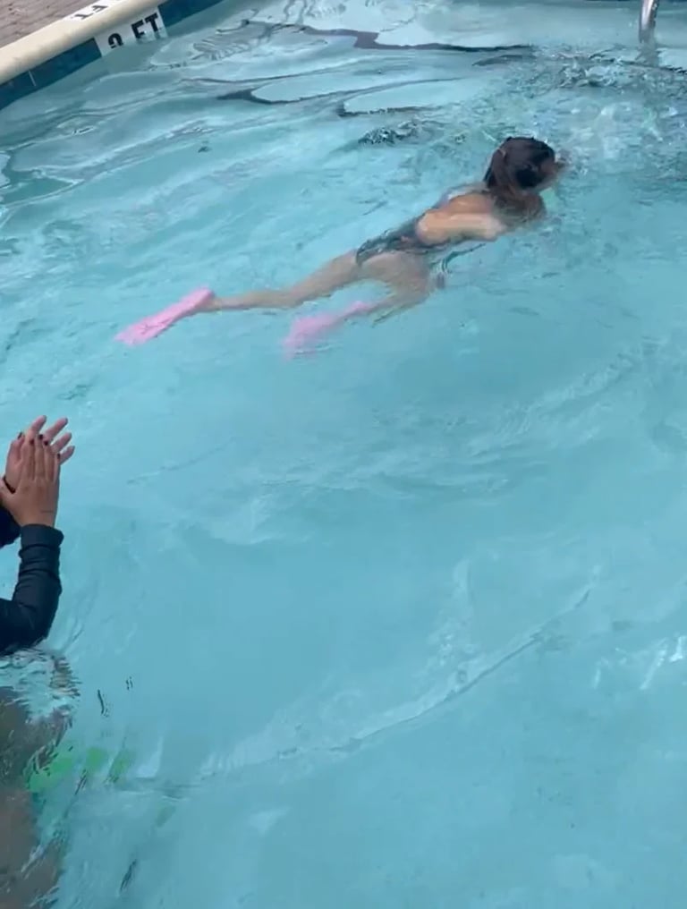 Child swimming with pink fins in a pool while instructor watches from the side
