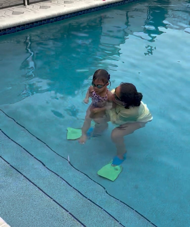 Adult and child in a swimming pool, child using green kickboards for swimming lessons instruction